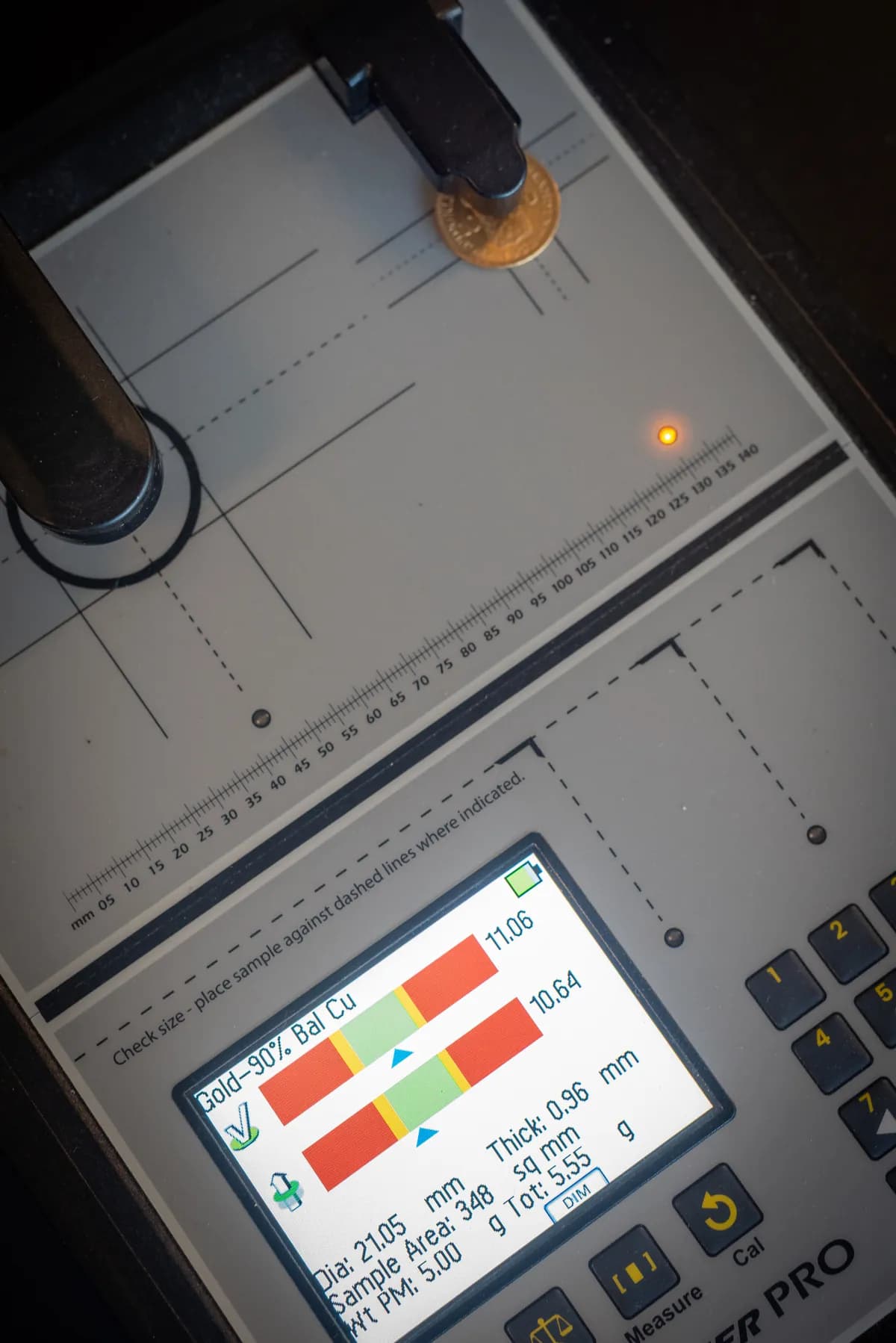 Het testapparaat van Sigma Metalytics in gebruik: een gouden munt ligt onder de meetpen en het scherm toont “Gold-90%” met de meting in het groene vlak.
